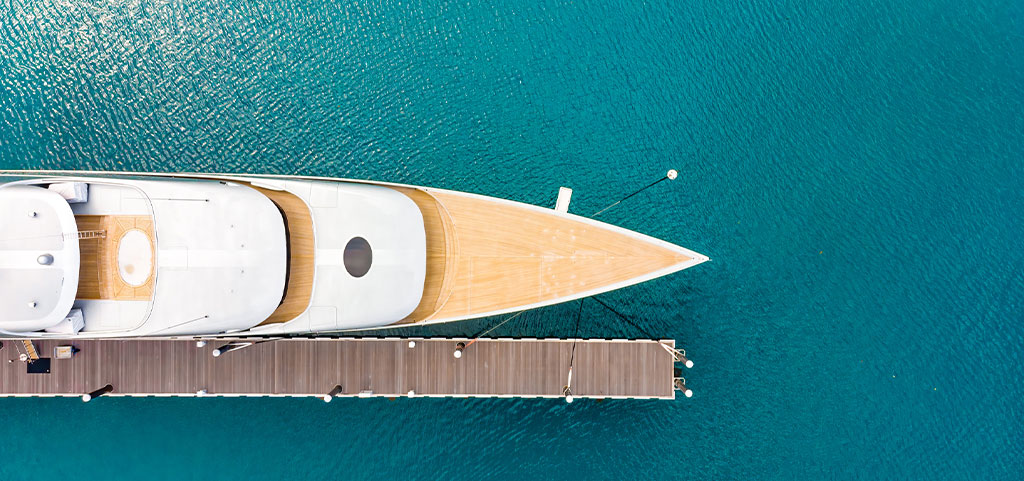 Vista aerea di un lussuoso yacht bianco moderno e costoso ormeggiato a un lungo molo in una baia con acque cristalline e turchesi dell'oceano. Avvicinamento. Concetto di turismo