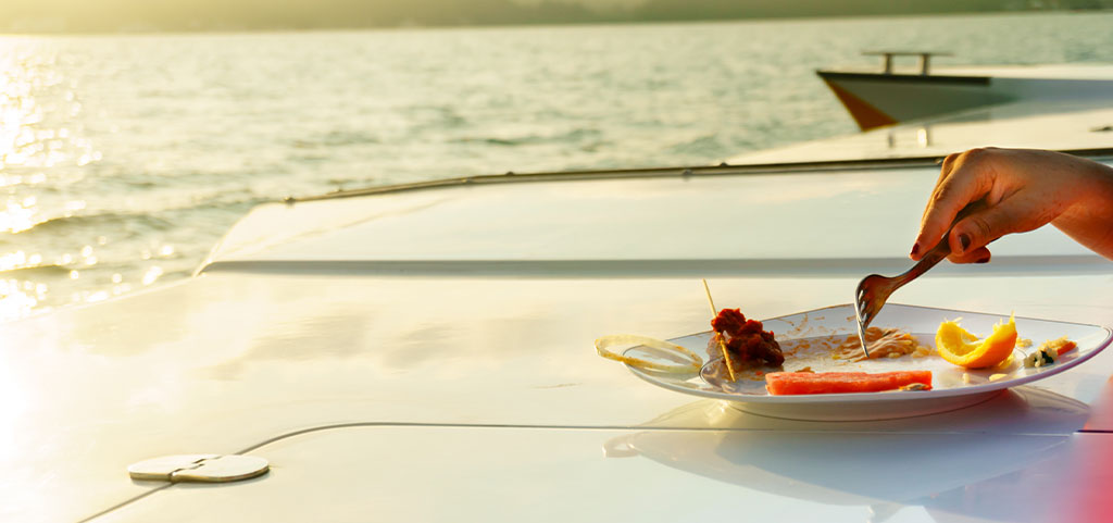 Mano con la forchetta che mangia cibo sul ponte di uno yacht. Un bellissimo riflesso dorato sull'obiettivo si aggiunge al tema ricco e ricco dello scatto
